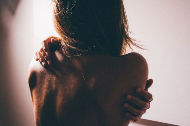 A close up photo of a woman hugging herself and grasping the muscles of her back. Photo by Romina Farías on Unsplash.